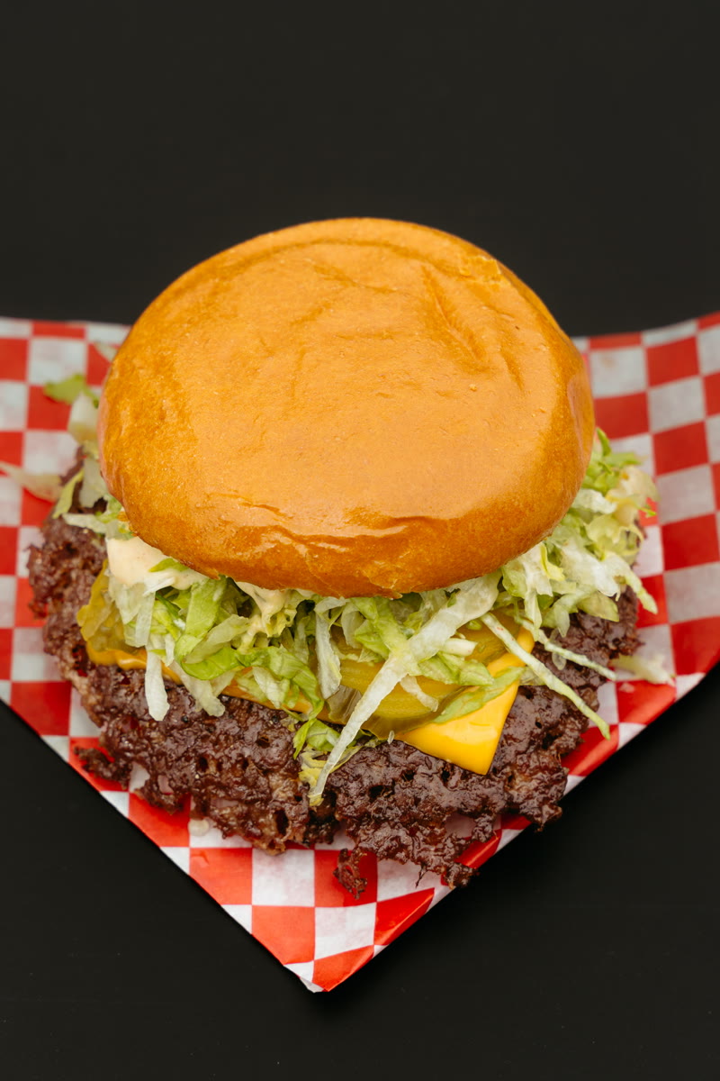 A Bud the Spud smash burger with pickle and cheese on checker paper