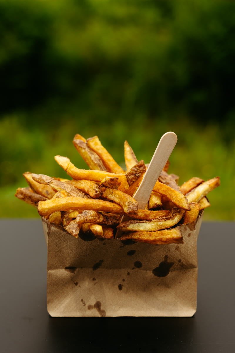 A kraft bag of hand-cut Bud the Spud fries against a green bokeh background