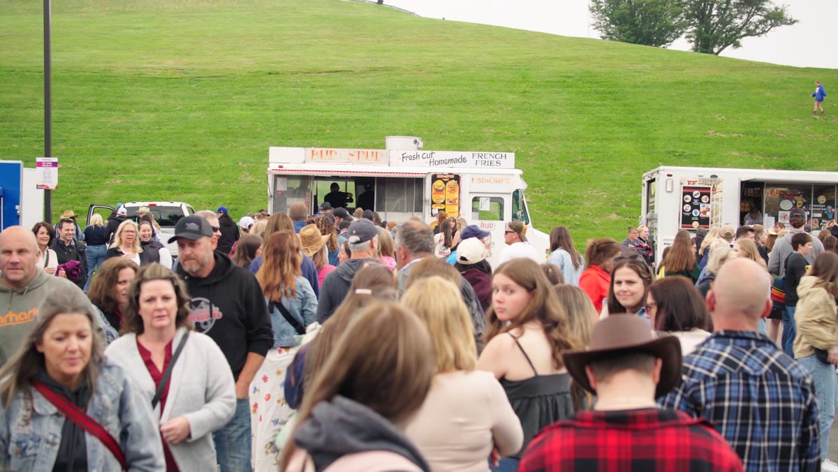 The BUDtheSPUD chip truck parked on a grassy field at an outdoor event, staff working the service window while a large crowd waits out front